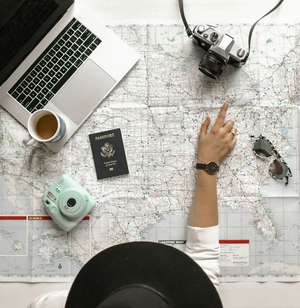 person planning a trip with a map, computer, camera, and passport